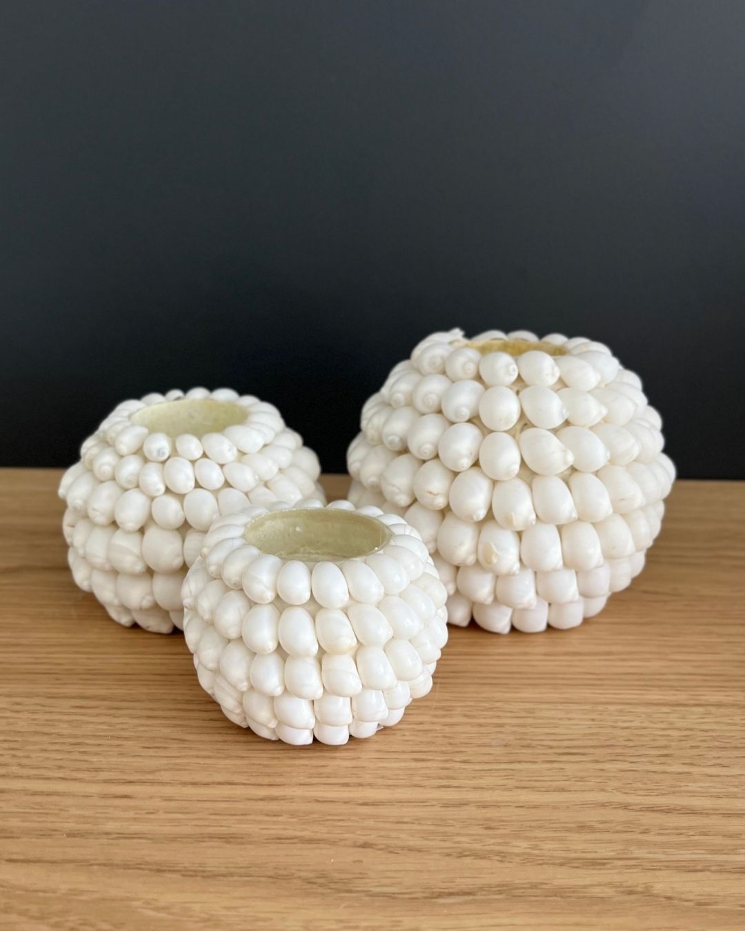 Three decorative candle holders made of white beads on a wooden surface with a black background.