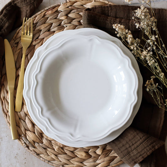 White ceramic plate on a woven placemat with gold fork and knife, and dried flowers.