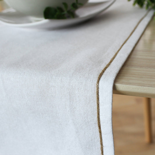 Close up of the non uniform organic texture of a beige recycled cotton runner showing the natural jute festoon border.