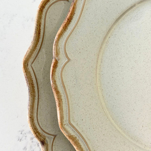 Close up of beige stoneware dessert plate with rustic glazed scalloped edge