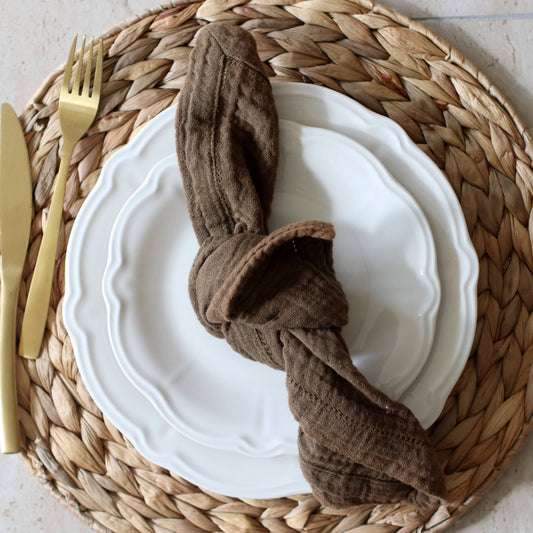 Gourmet cake presentation on a Charlotte 20cm white stoneware plate, modern Mediterranean style with a brown napkin, gold fork, and knife on a woven placemat.