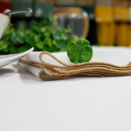Close up of the dark beige jute festoon border on a natural sand colored napkin showing the organic recycled fabric texture.