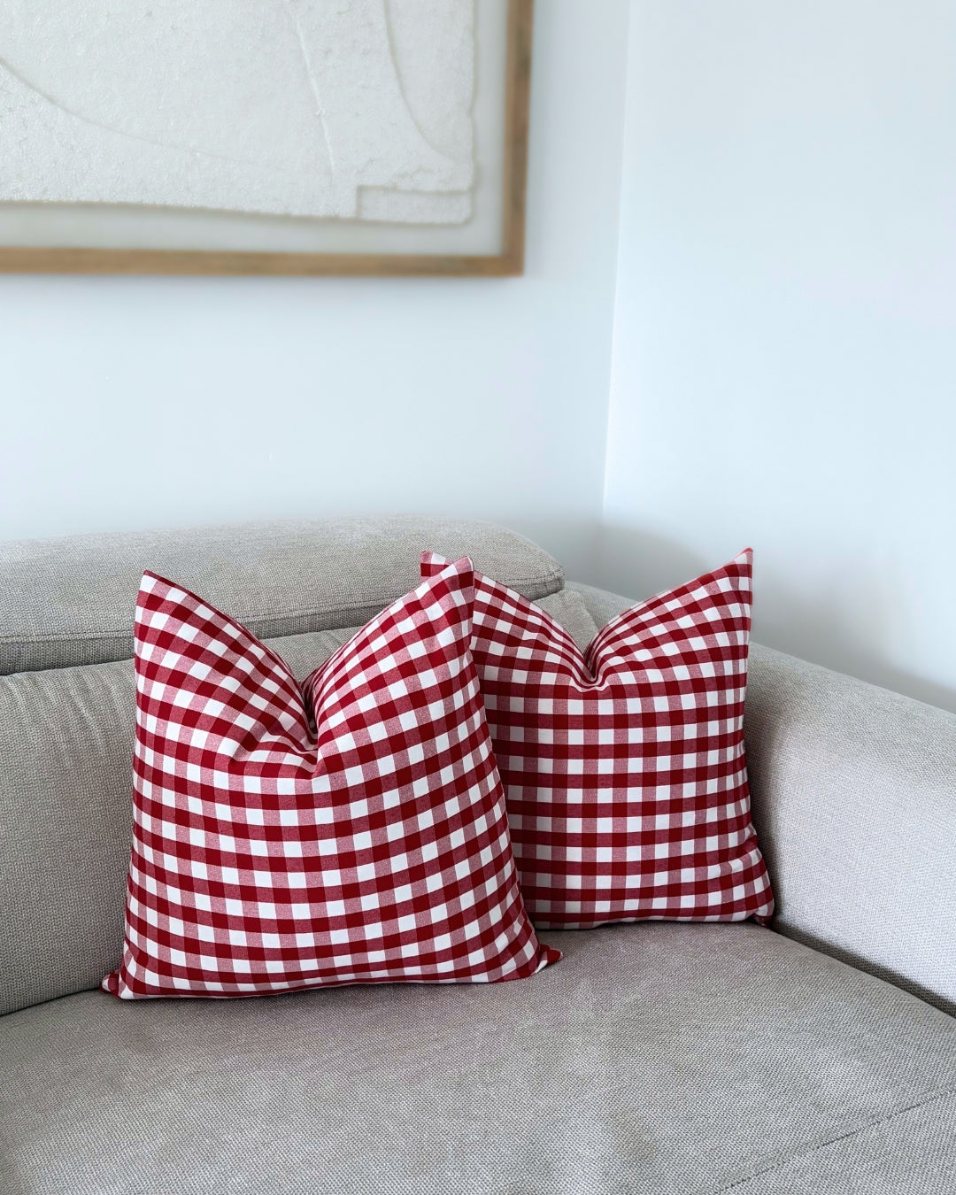 Two red check cushion covers styled on a beige sofa with warm autumn and Halloween home decor accents.