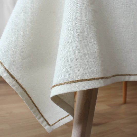 Close-up of recycled cotton fabric texture and hand-finished jute festoon border on beige tablecloth