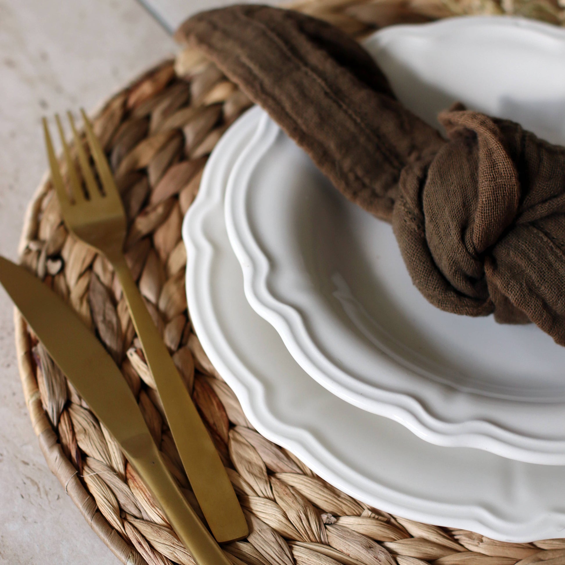White plates with gold cutlery and a brown napkin on a woven placemat.