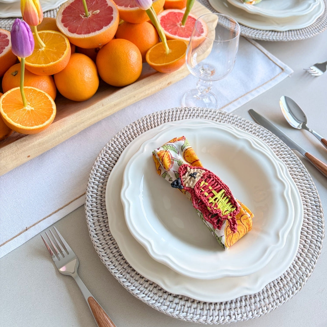 Table setting with a decorative plate, colorful napkin, and fresh fruit on a white table.