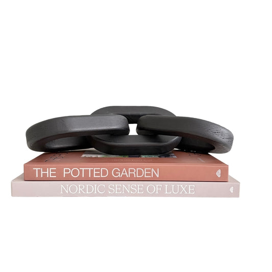 A sculptural black interlocking ring chain decoration displayed on top of two stacked books against a plain white background.