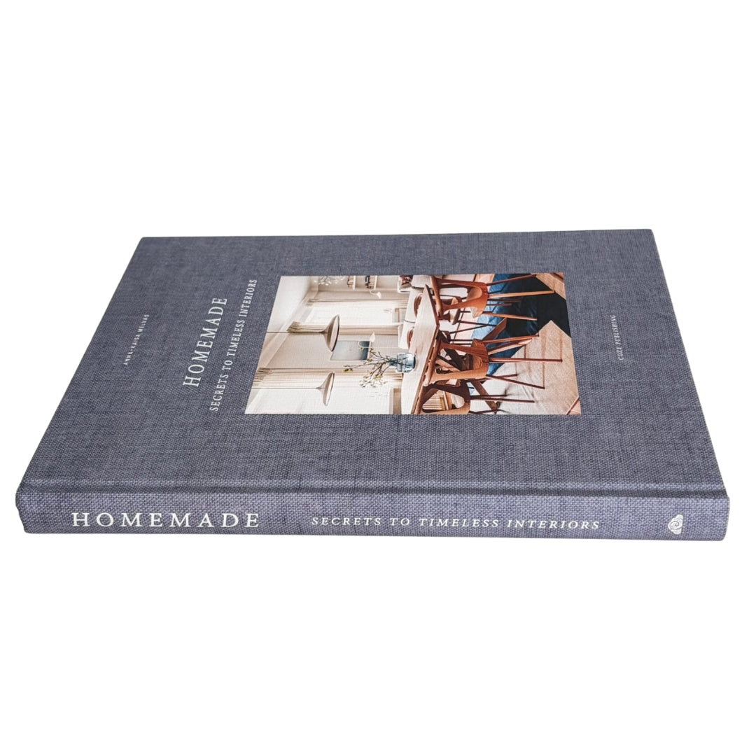 A hardcover book titled 'Homemade: Secrets to Timesless Interiors' with a textured dark gray-blue cover and a central interior design photograph, shown on a plain white background.
