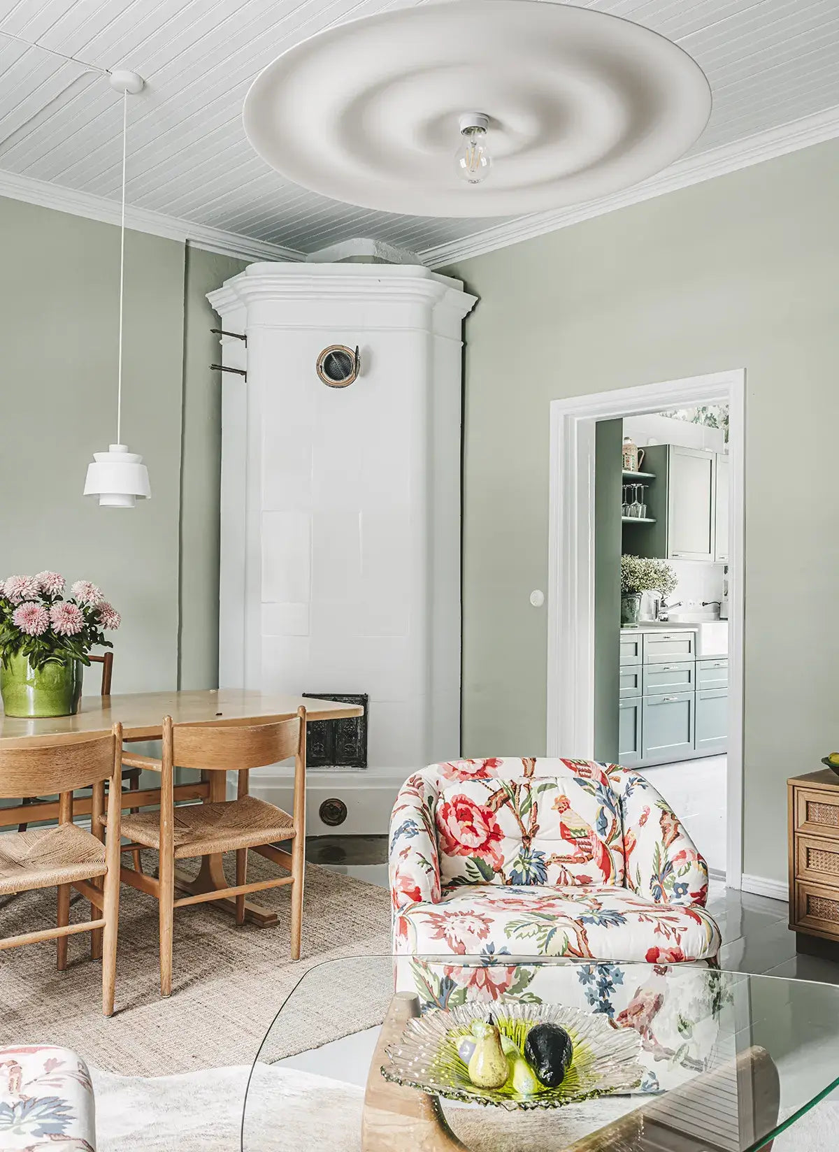 Living room with floral armchair, dining table, and kitchen in the background.