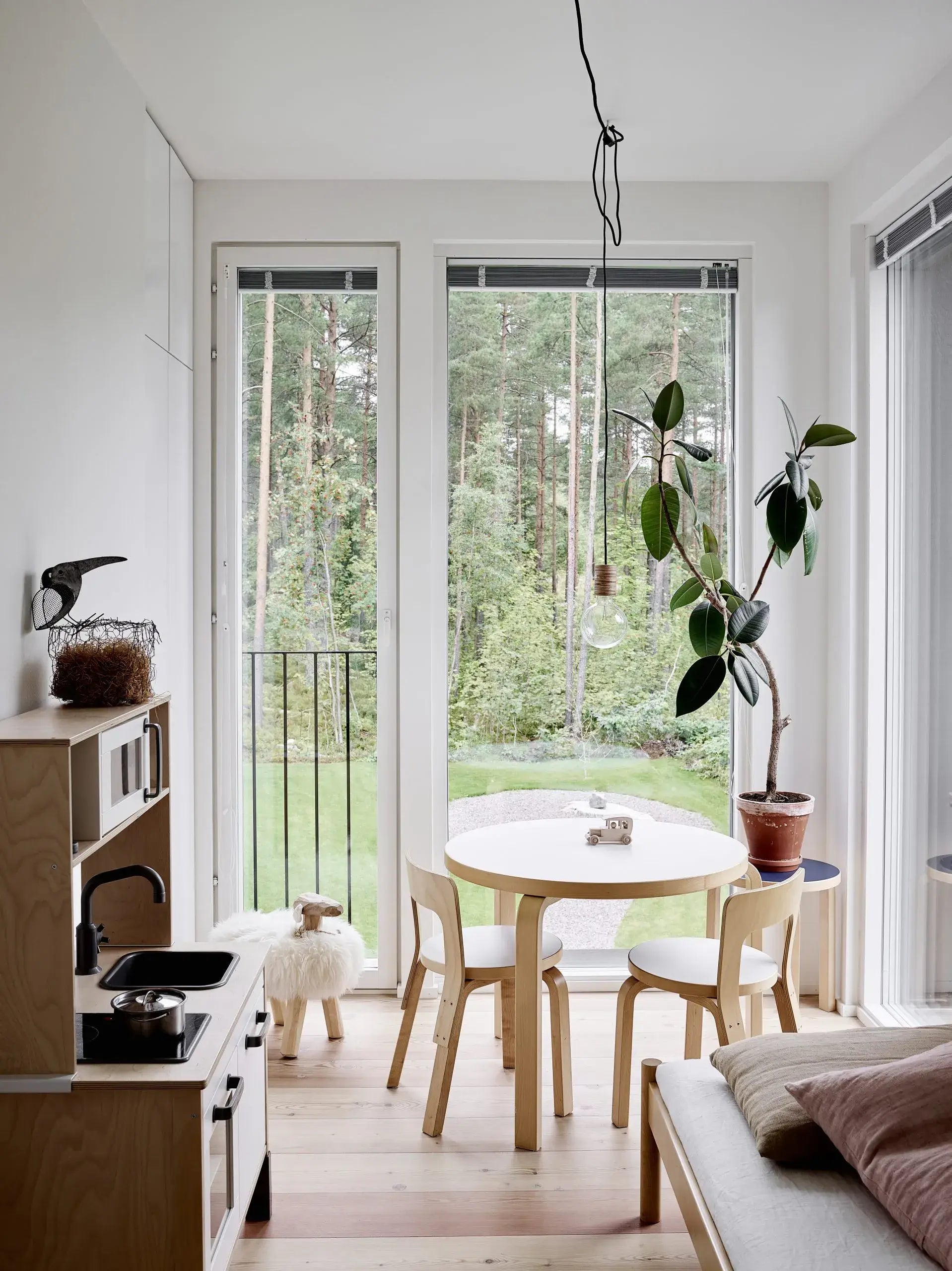 Modern kitchen with a round dining table and chairs, large windows, and a view of greenery outside.