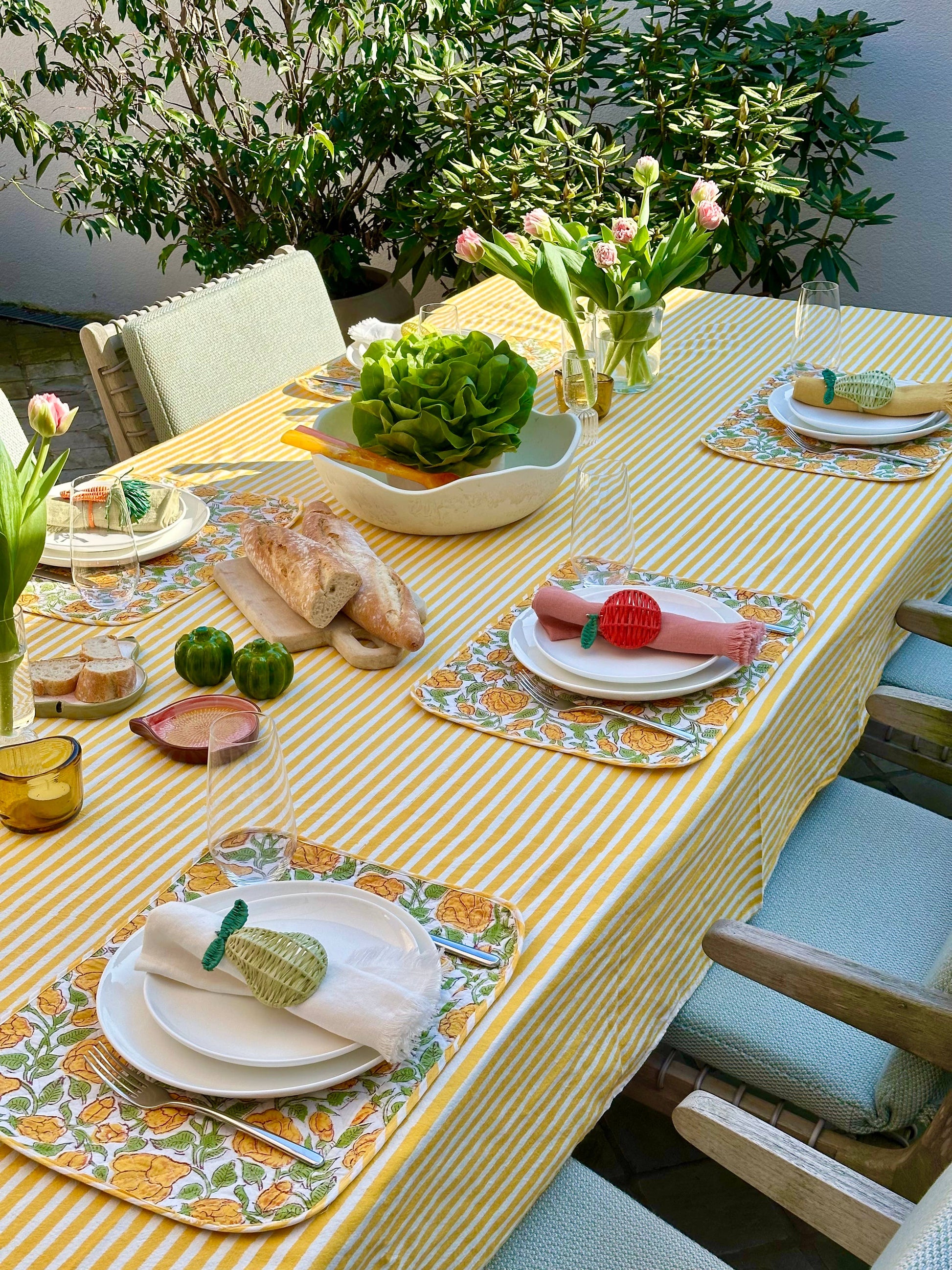 Outdoor dining table set with yellow checkered tablecloth, floral arrangements, and decorative plates.