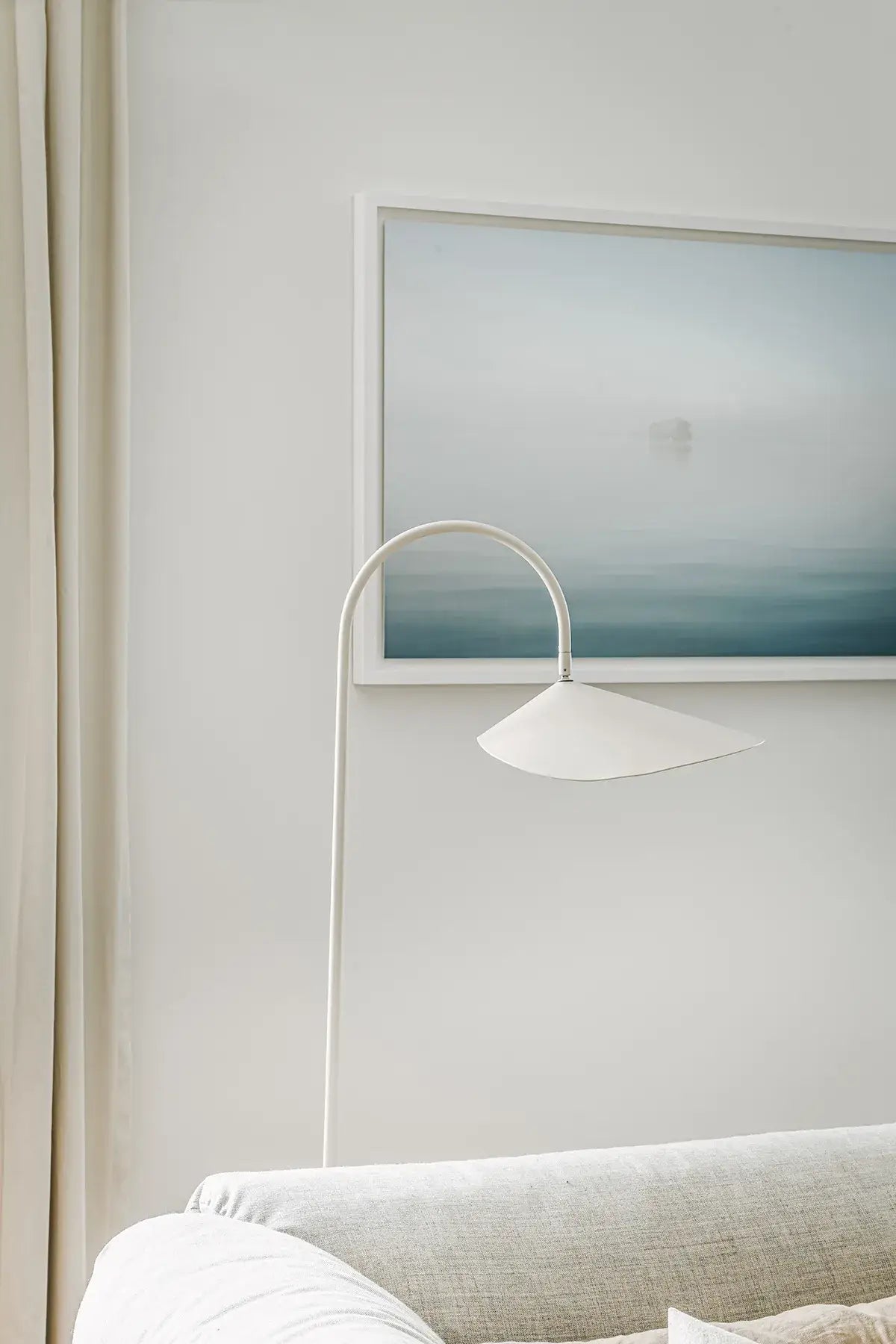 Modern floor lamp next to a framed abstract painting on a white wall.