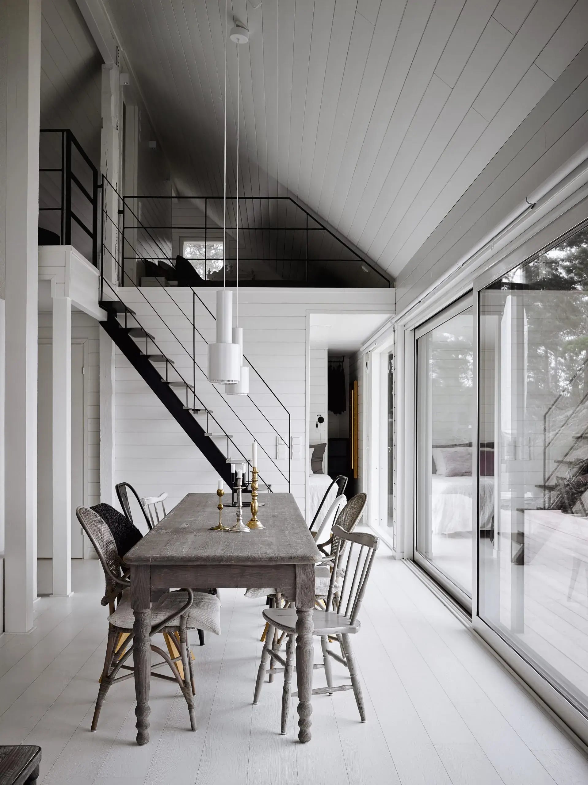 Modern interior with a dining table and chairs near a staircase and large windows.