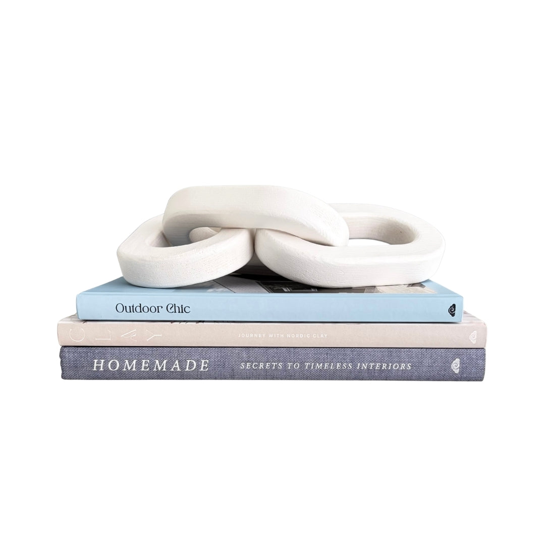 A white ceramic decorative knot sculpture displayed on top of a stack of three books against a solid white background.