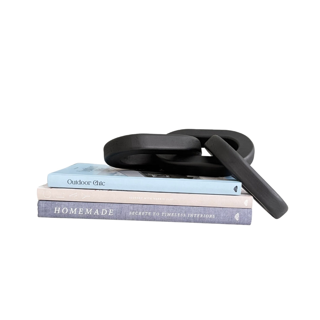 A black silicone kitchen utensil, likely a small whisk or turner, resting on top of two stacked books on a plain white background.