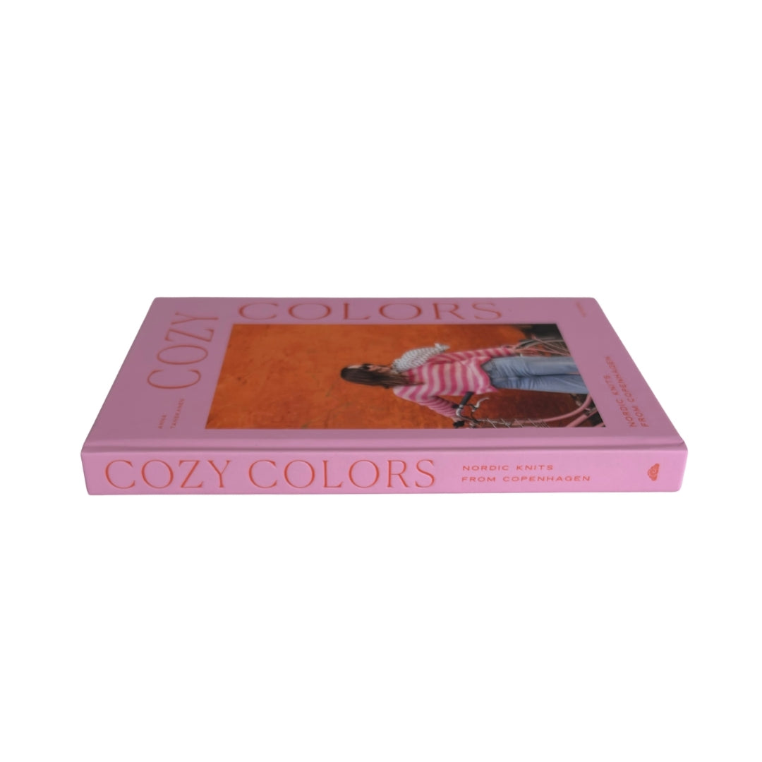 A pink hardcover book titled 'COZY COLORS' with a central cover photograph of a person in a striped shirt, shown on a plain white background.
