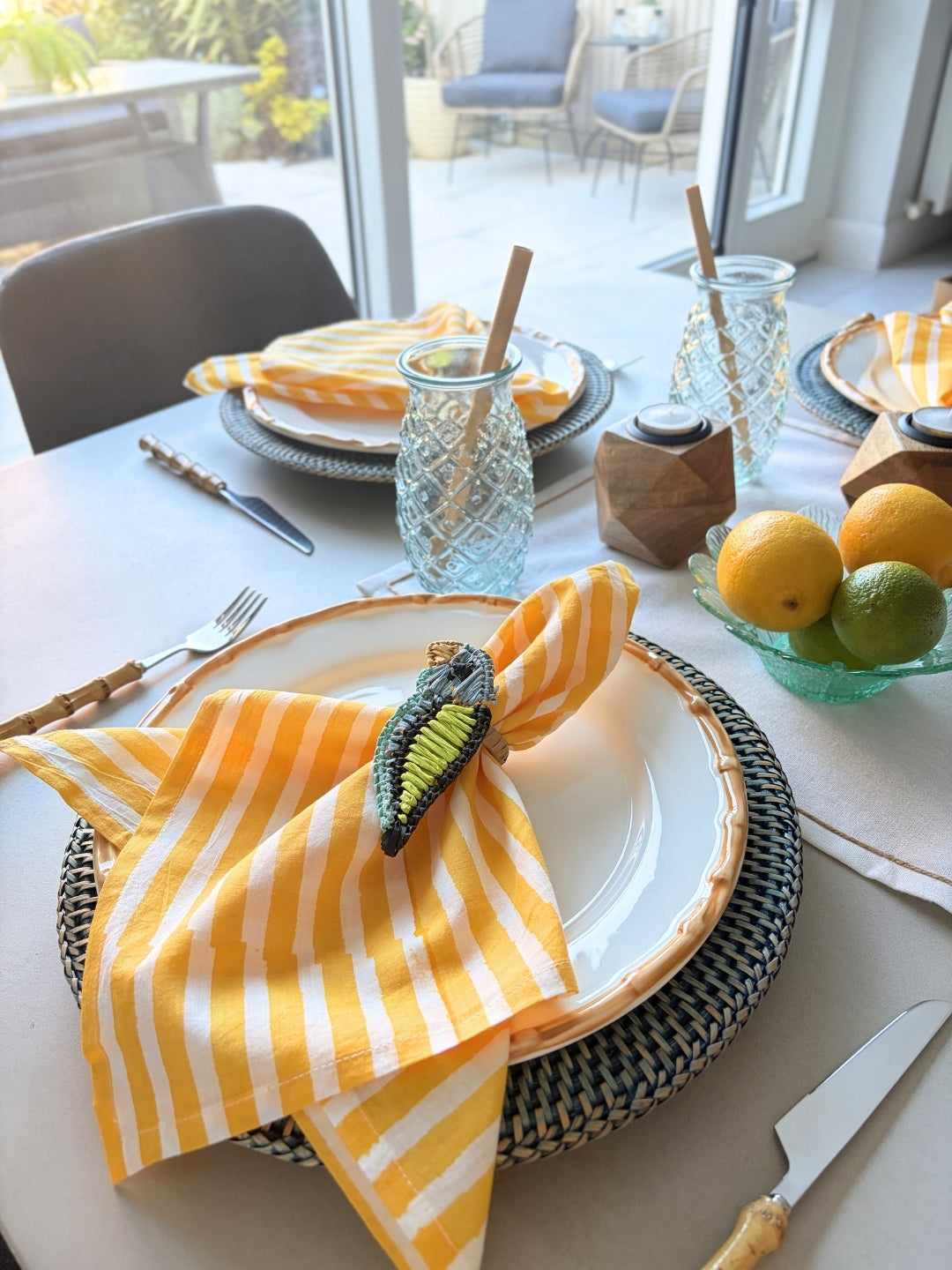 Dining table setting with yellow and white striped napkin, glassware, and fruit on a white tablecloth.