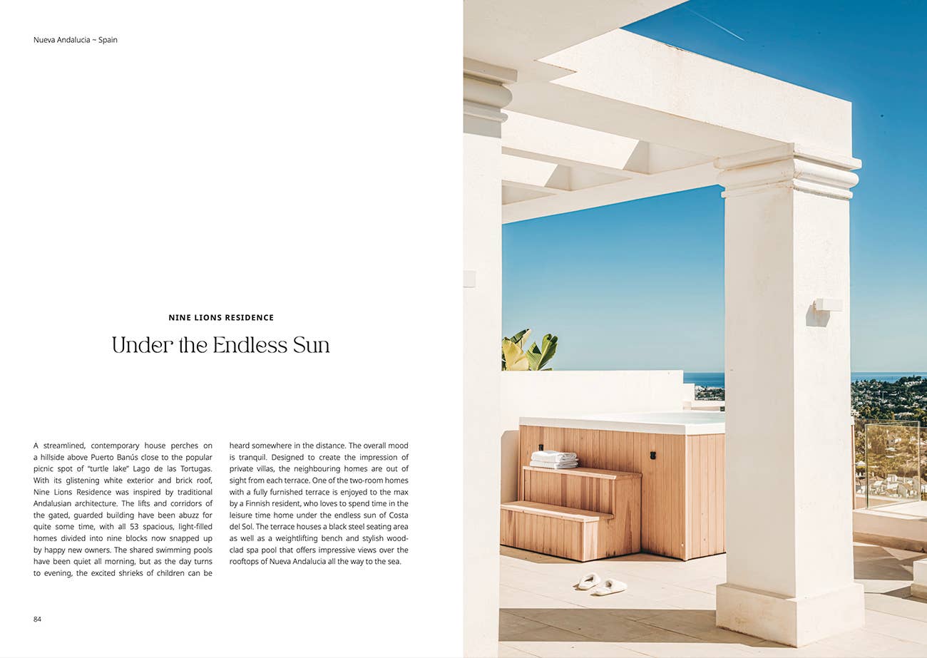 Modern outdoor living space with white columns and wooden furniture, set against a clear blue sky.