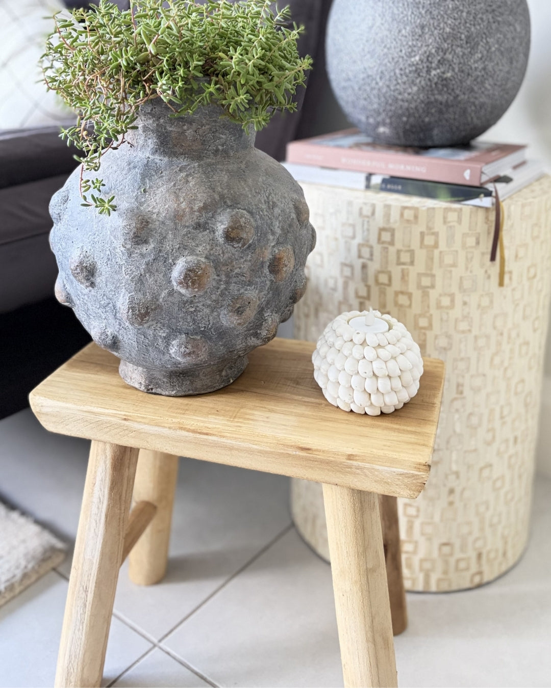 Decorative stone vase with plants on a wooden stool in a home setting