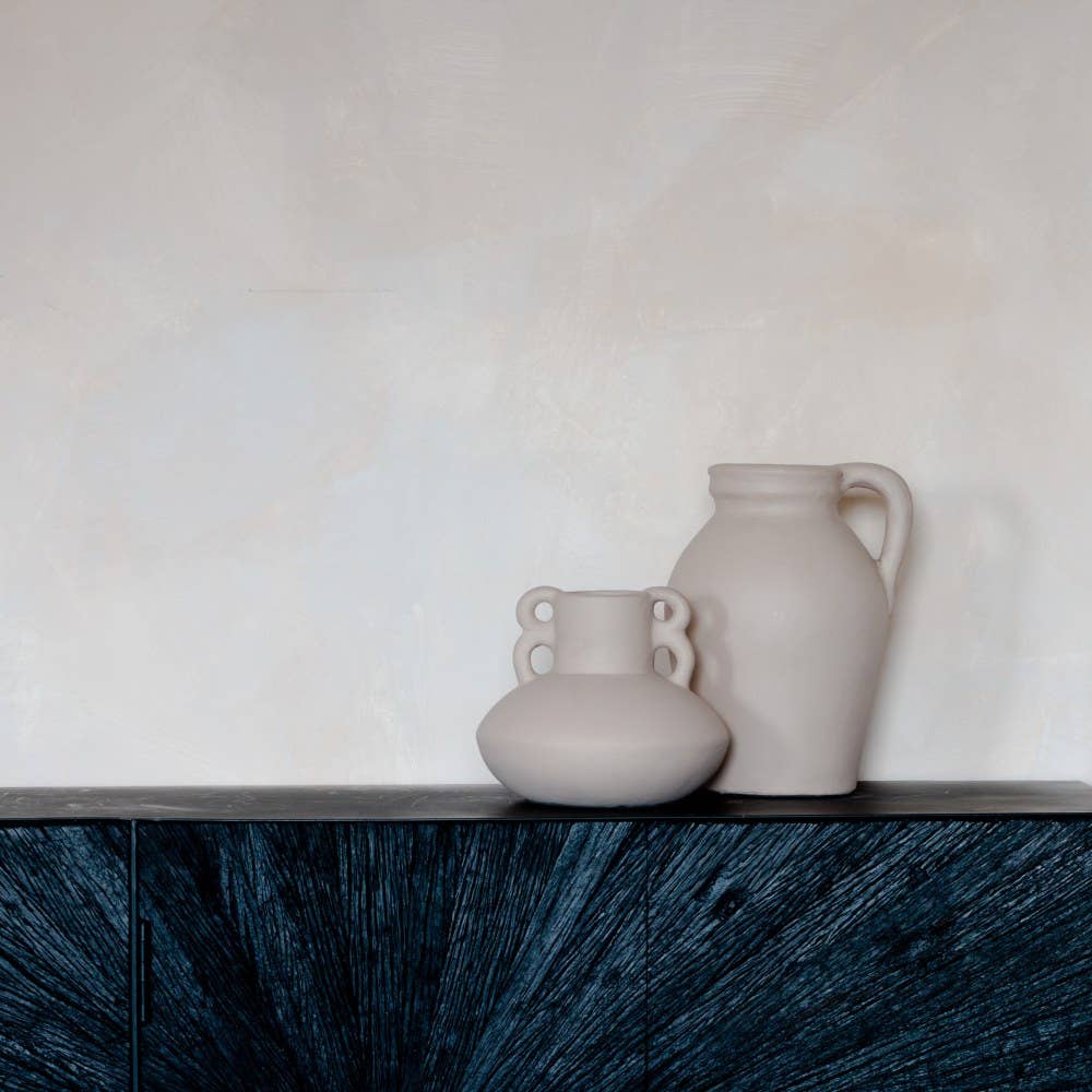 Two ceramic vases on a dark wooden surface with a light background. Emi 2-handle sculptural terracotta vase 19cm and Emi 1 handle vases 27cm.