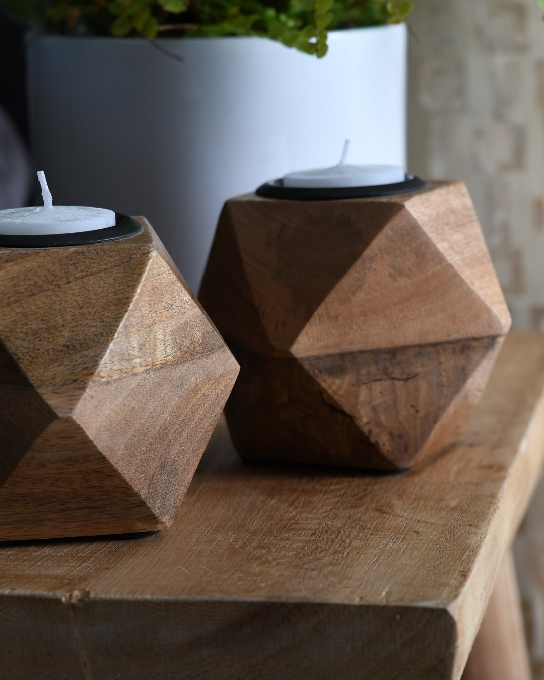 Two geometric wooden candle holders on a wooden surface with a blurred background.
