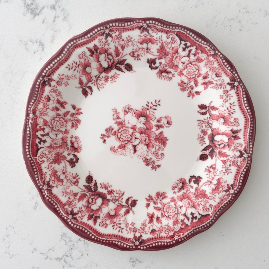 Faustine antique red floral dinner plate displayed on a cream-toned pedestal, highlighting the romantic 2026 Antique Rose trend and high-gloss finish.