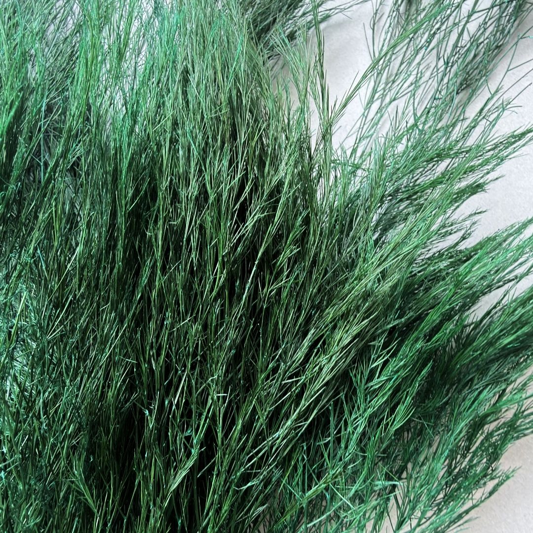 A dense bundle of artificial green grass or ornamental grass strands, photographed close-up against a light neutral background.