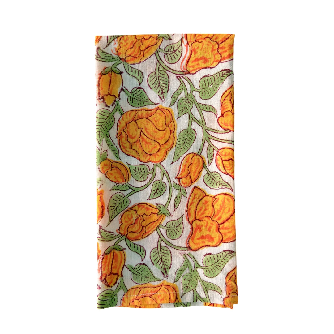 Close up of the artisanal botanical hand-block print in orange, golden yellow and moss green on a 100% white cotton napkin.