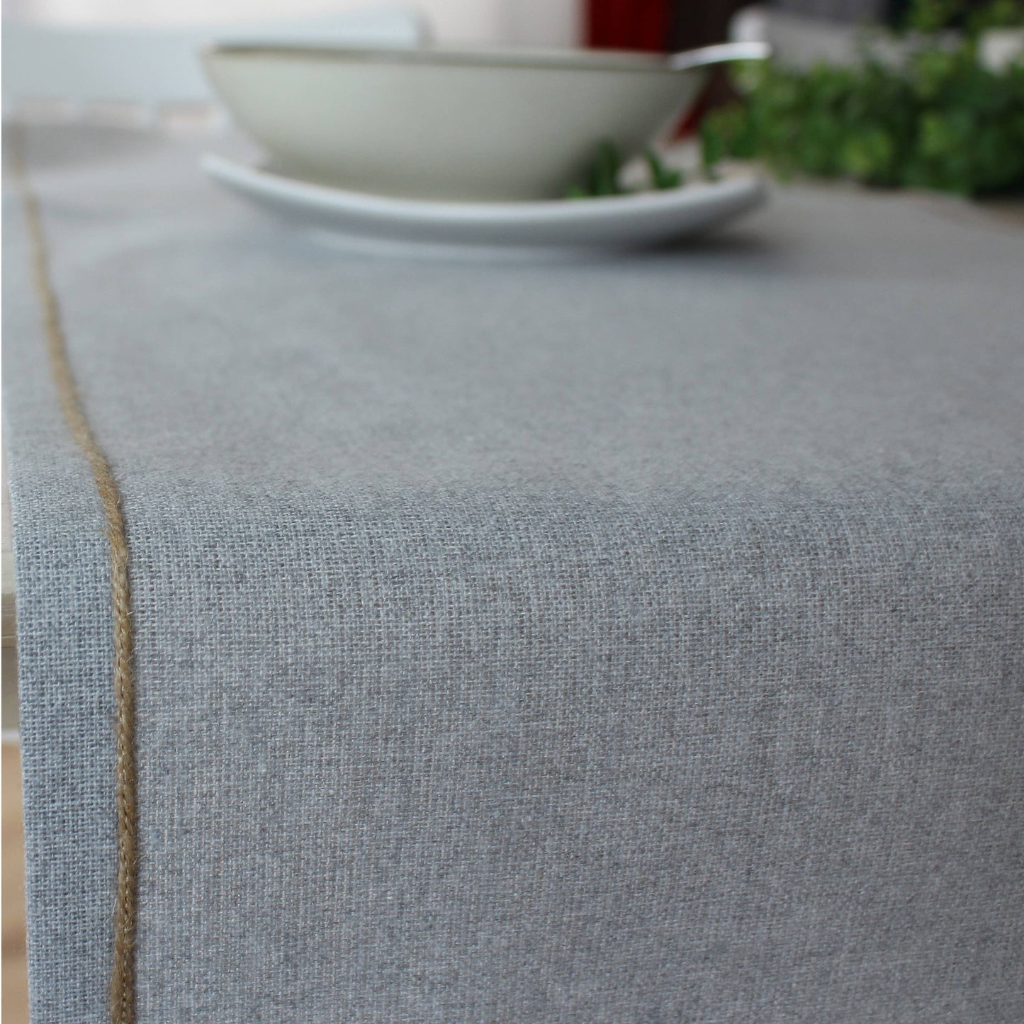 Close up of the artisanal jute festoon border against the soft ash grey recycled fabric of a modern table runner.