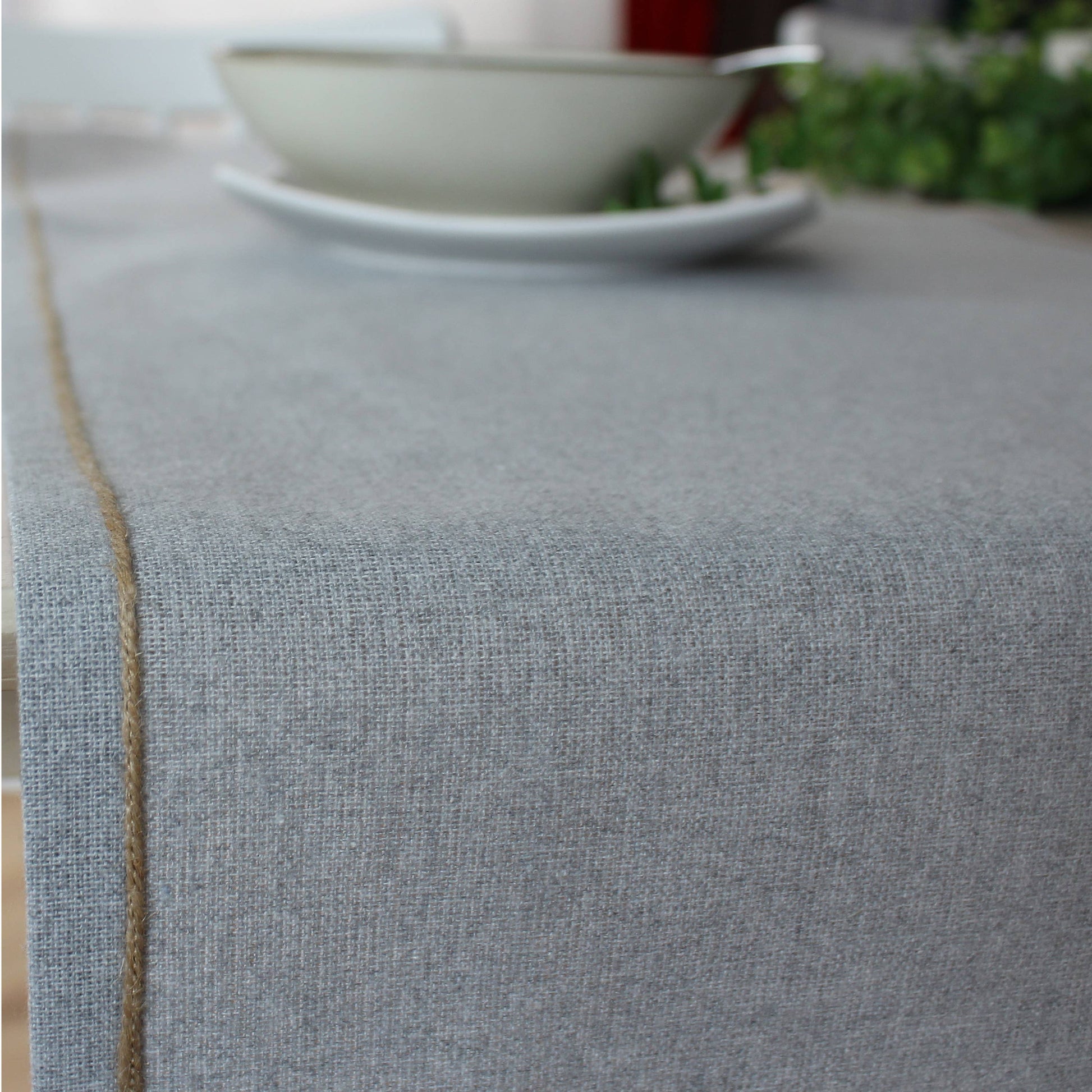 Close up of the artisanal jute festoon border against the soft ash grey recycled fabric of a modern table runner.
