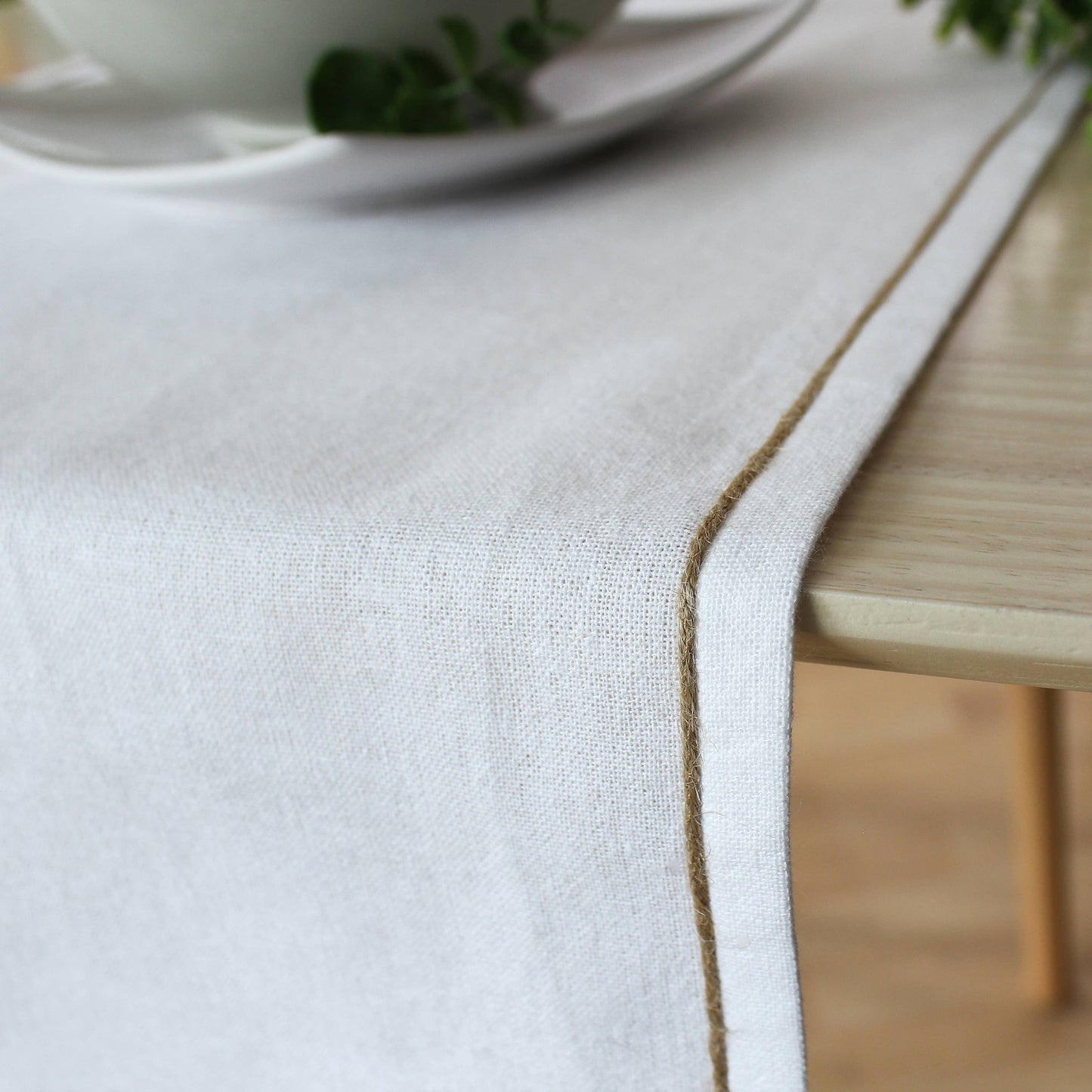 Close up of the non uniform organic texture of a beige recycled cotton runner showing the natural jute festoon border.