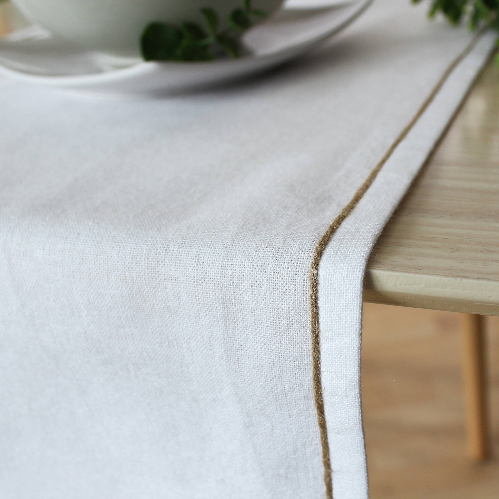 Close up of the non uniform organic texture of a beige recycled cotton runner showing the natural jute festoon border.
