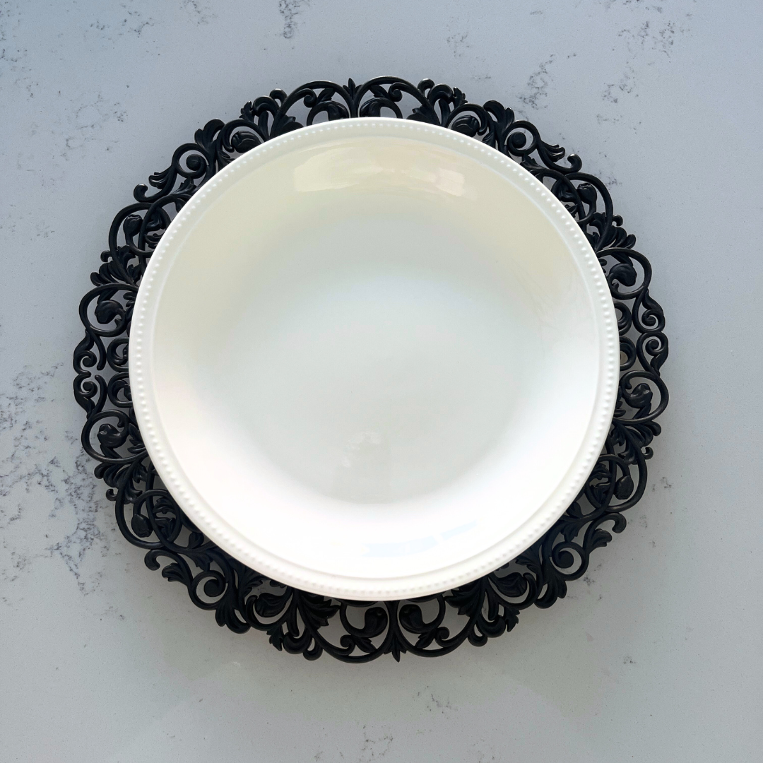 Black ornamental charger plate beneath white dinnerware for a sophisticated table setting