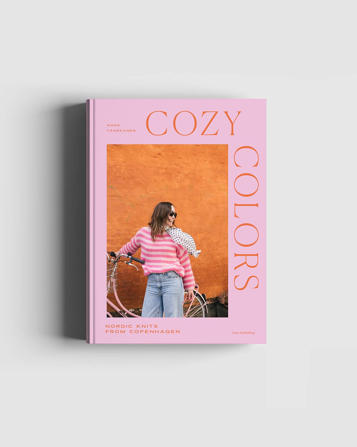 Book titled 'Cozy Colors' with a woman on a bike on the cover against a pink background