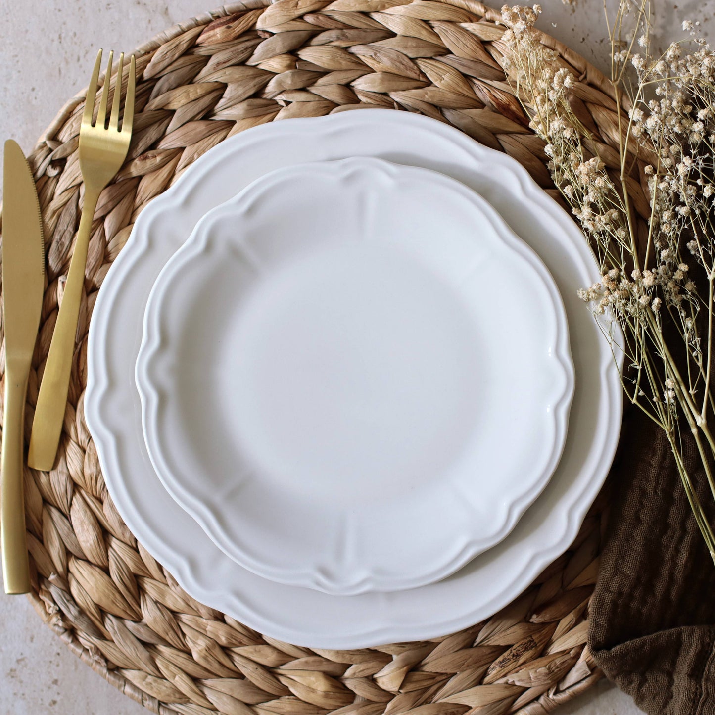 White ceramic plate on a woven placemat with gold fork and knife, and dried flowers.