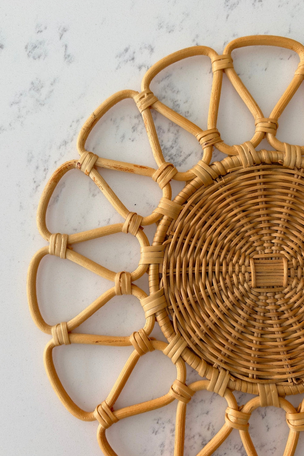 Close-up detail of the natural woven rattan placemat with scalloped circular border on a light marble surface.