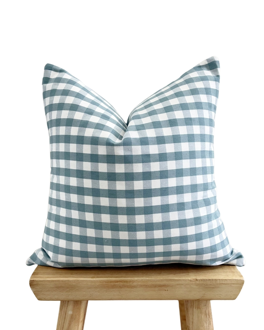 Blue and white checkered pillow on a wooden stool against a white background