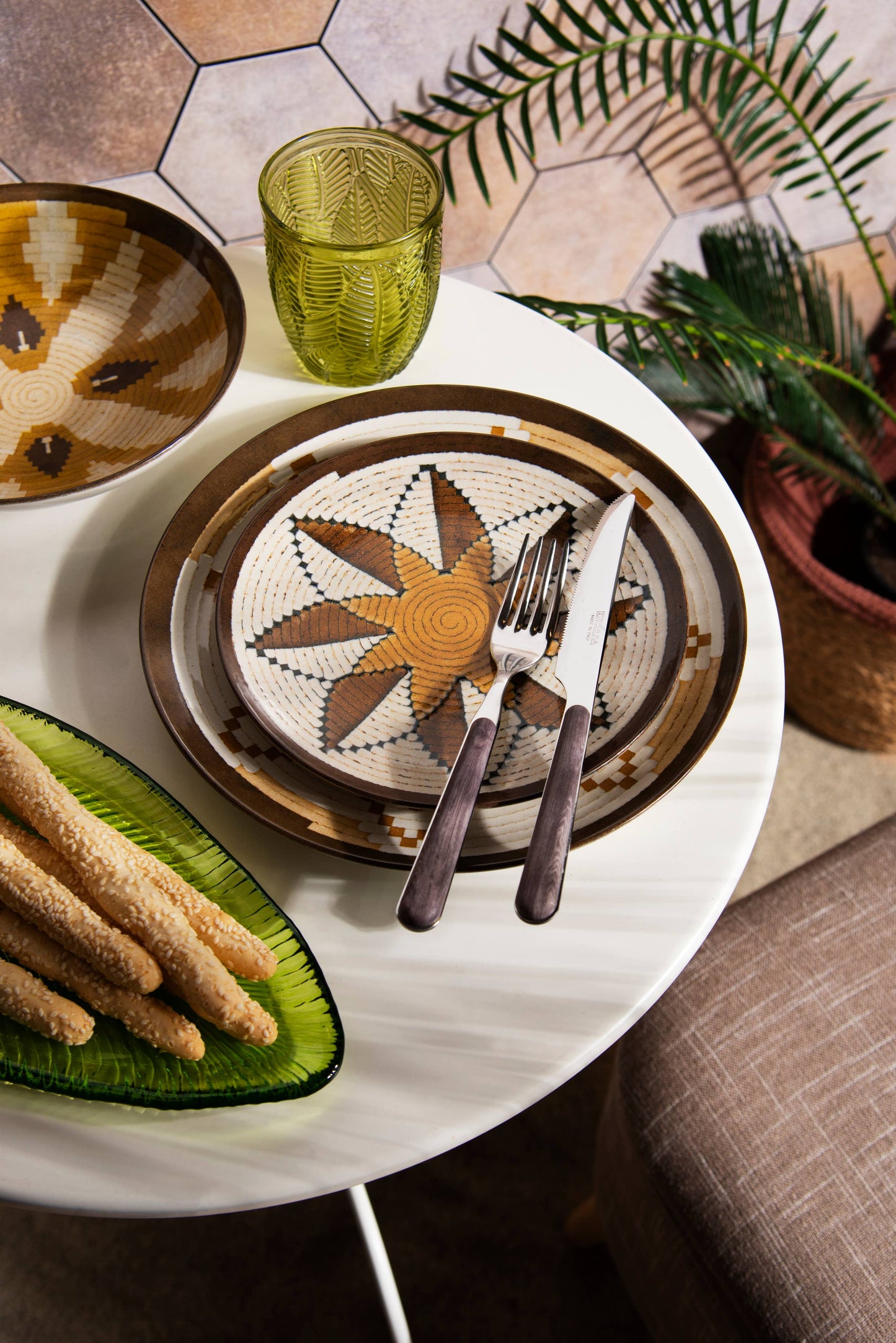 Table setting with decorative plates, cutlery, and a glass on a white table.