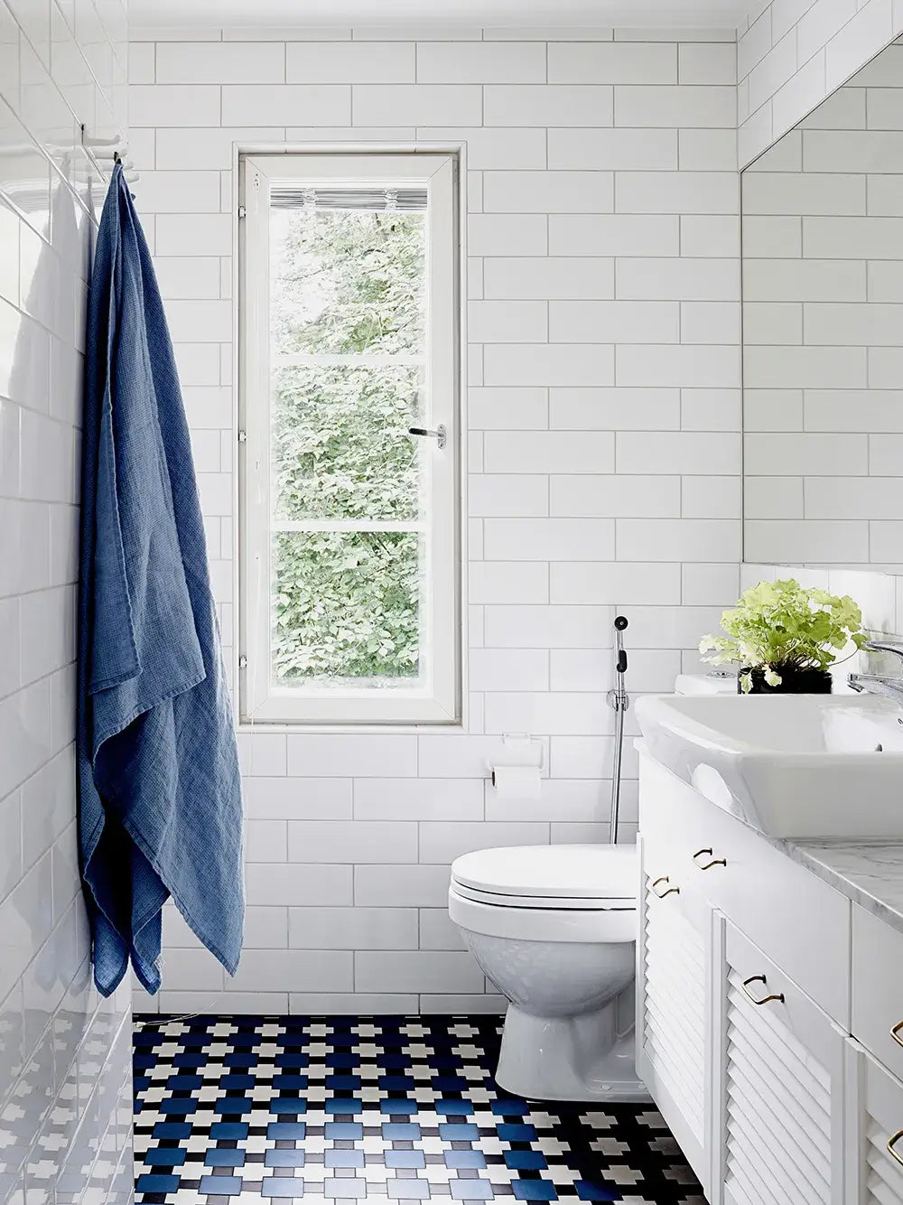 Bathroom with white tiled walls, a window, a toilet, and a sink with a blue towel hanging.