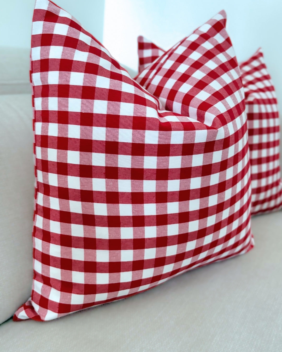 Set of 2 red gingham cushion covers on beige sofa for Christmas and festive holiday living room decor.