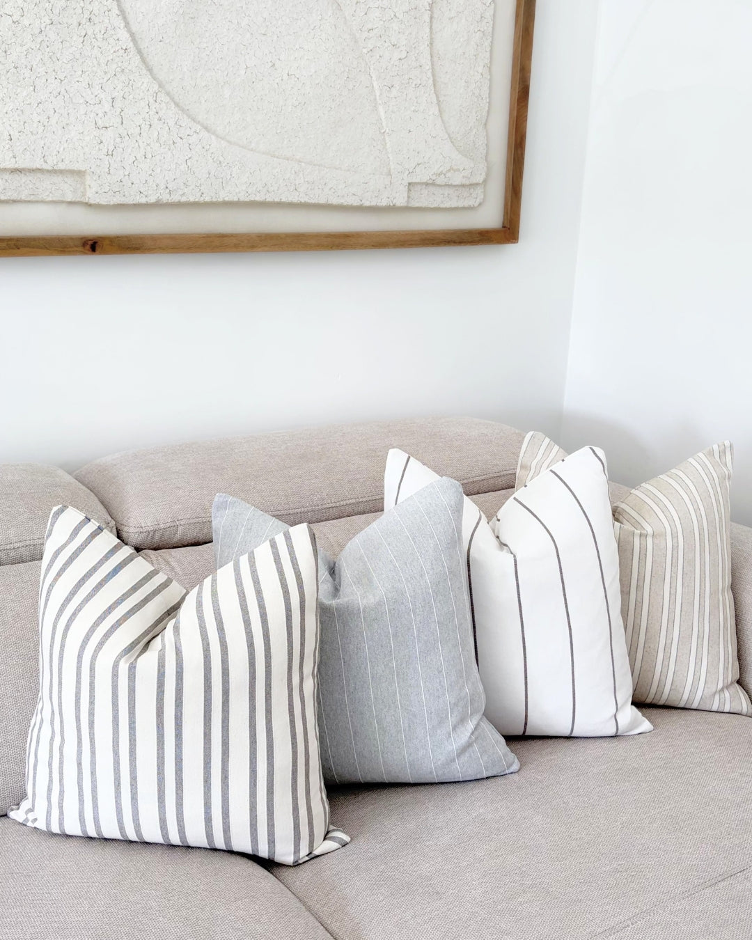 Arrangement of four grey and white linear textured cushions on a beige designer sofa.