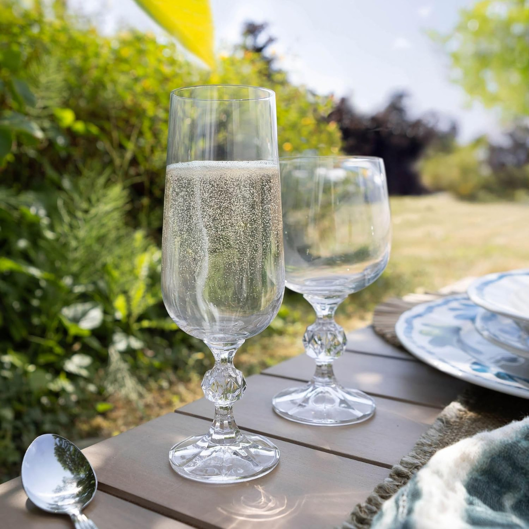 Two glasses of sparkling wine on a wooden table outdoors with greenery in the background