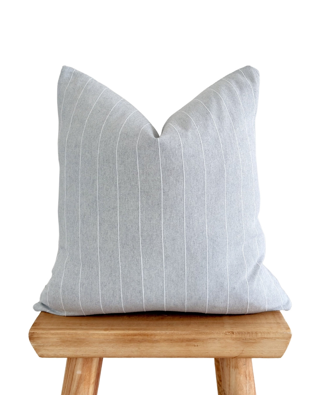 Grey linear jacquard cushion cover styled on a rustic wooden stool.
