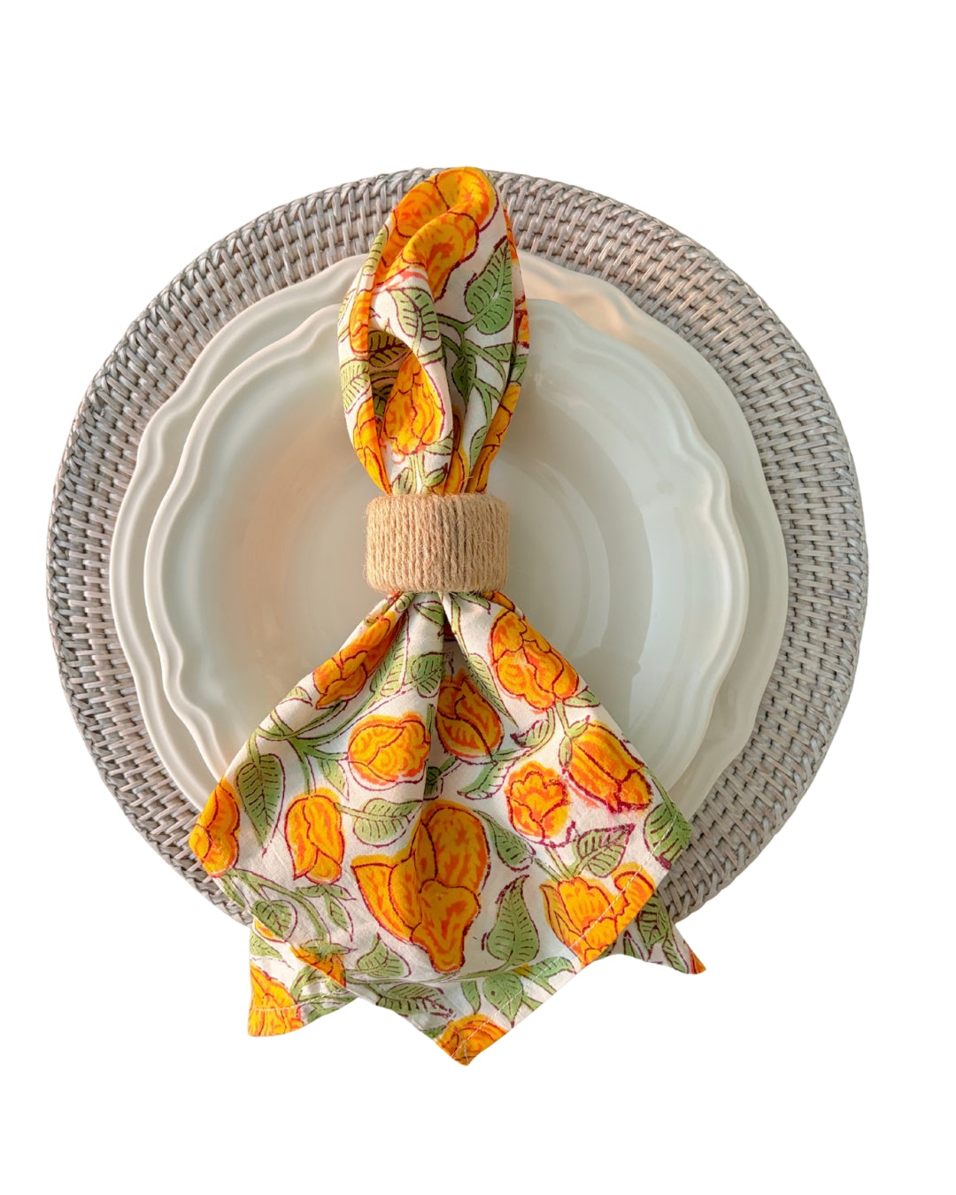 Decorative napkin with orange floral pattern on a white plate with a wihite rattan woven charger.