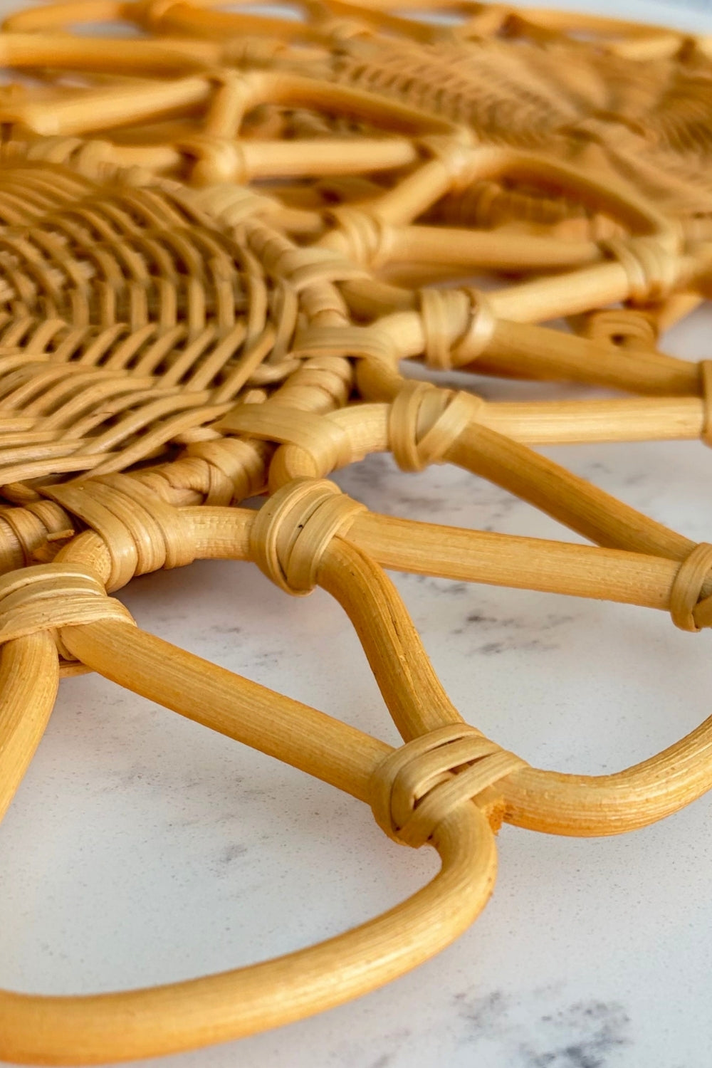 Close-up of natural light rattan woven geometric texture resting on a white marble surface.