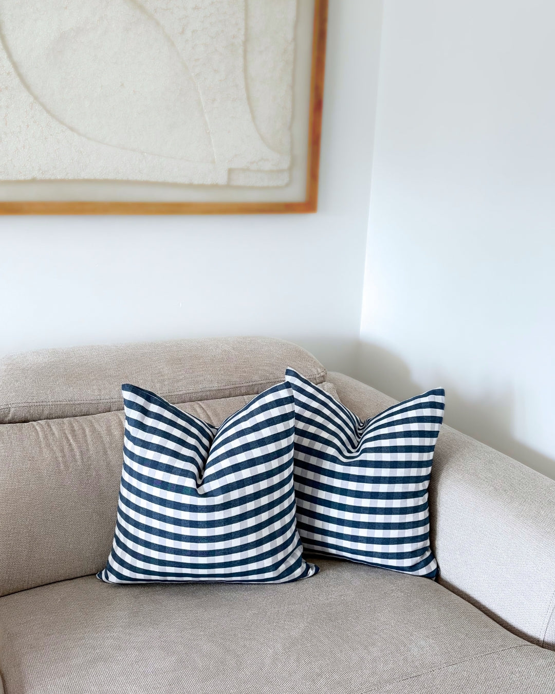 Two navy blue check cushion covers styled on a beige sofa with warm autumn and Halloween home decor accents.