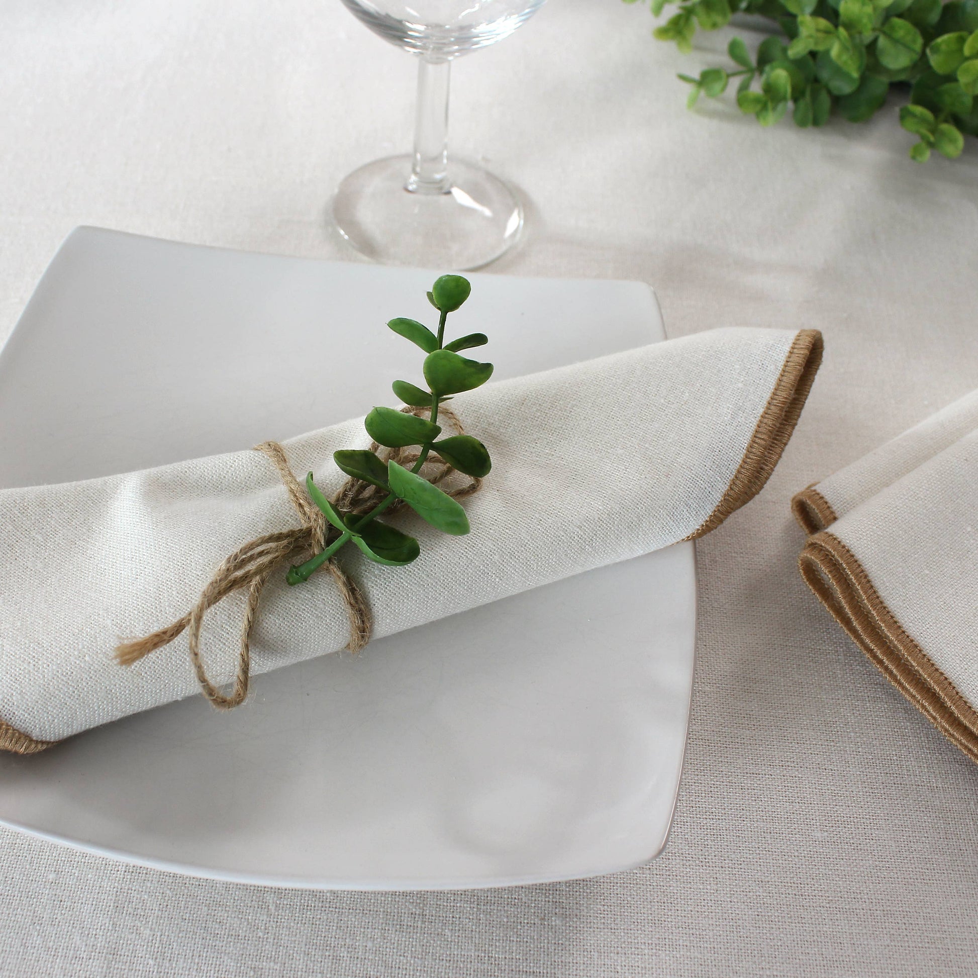 Organic modern table setting with natural beige napkins and jute trim on a rustic wooden dining table.