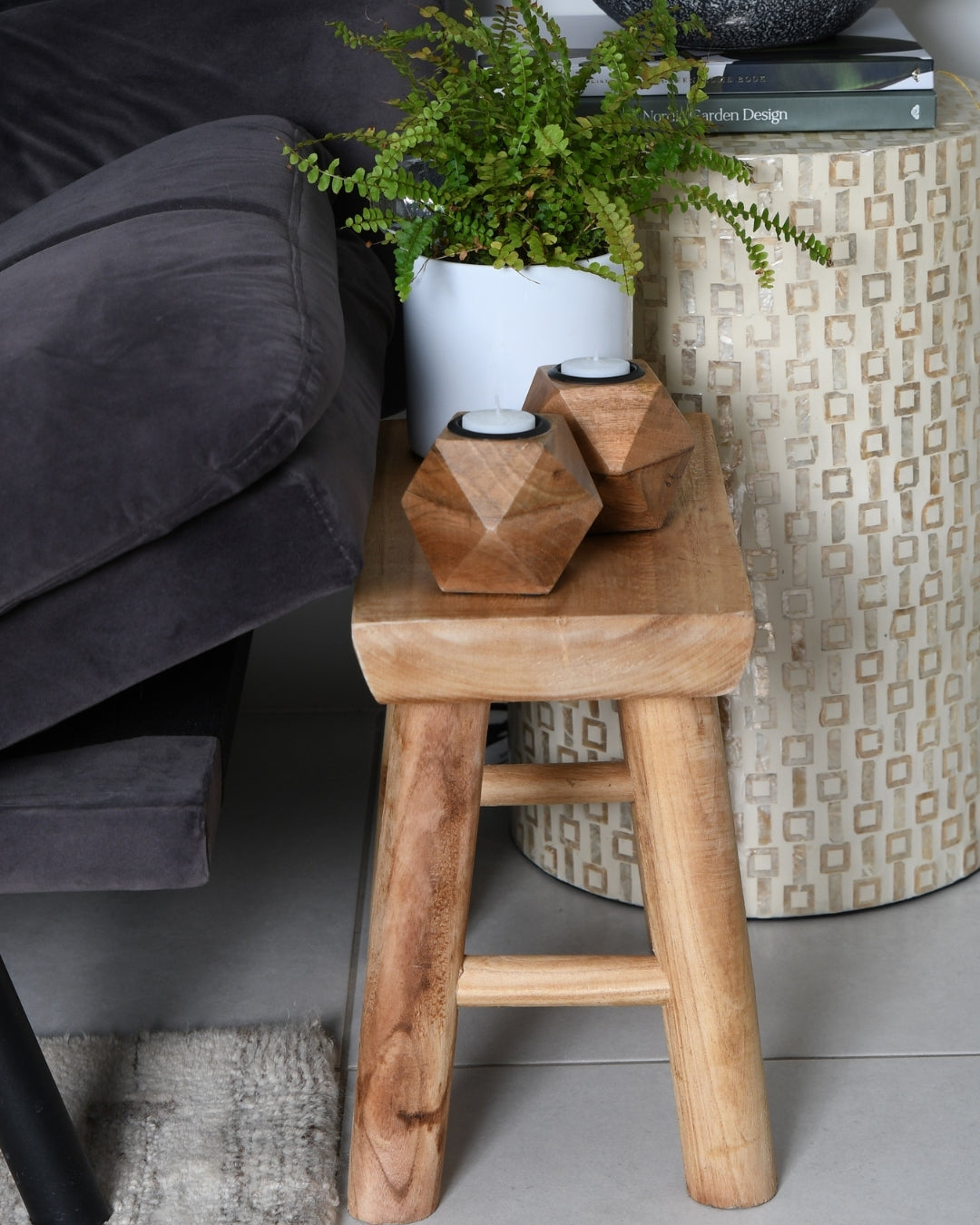 Raw wood artisan stool used as a decorative side table in a bright, modern living room.