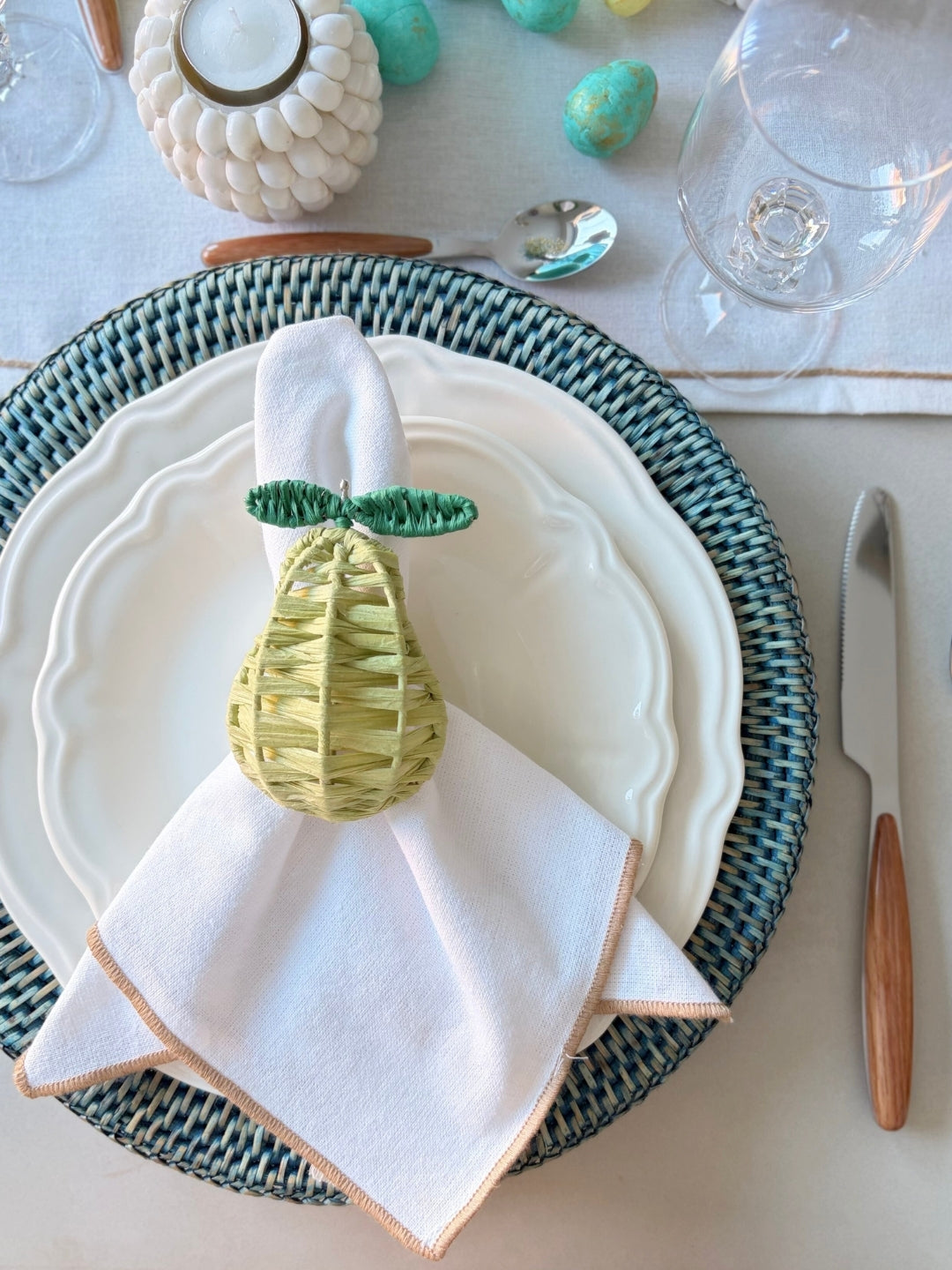 Table setting with a decorative pear-shaped napkin holder on a white plate.