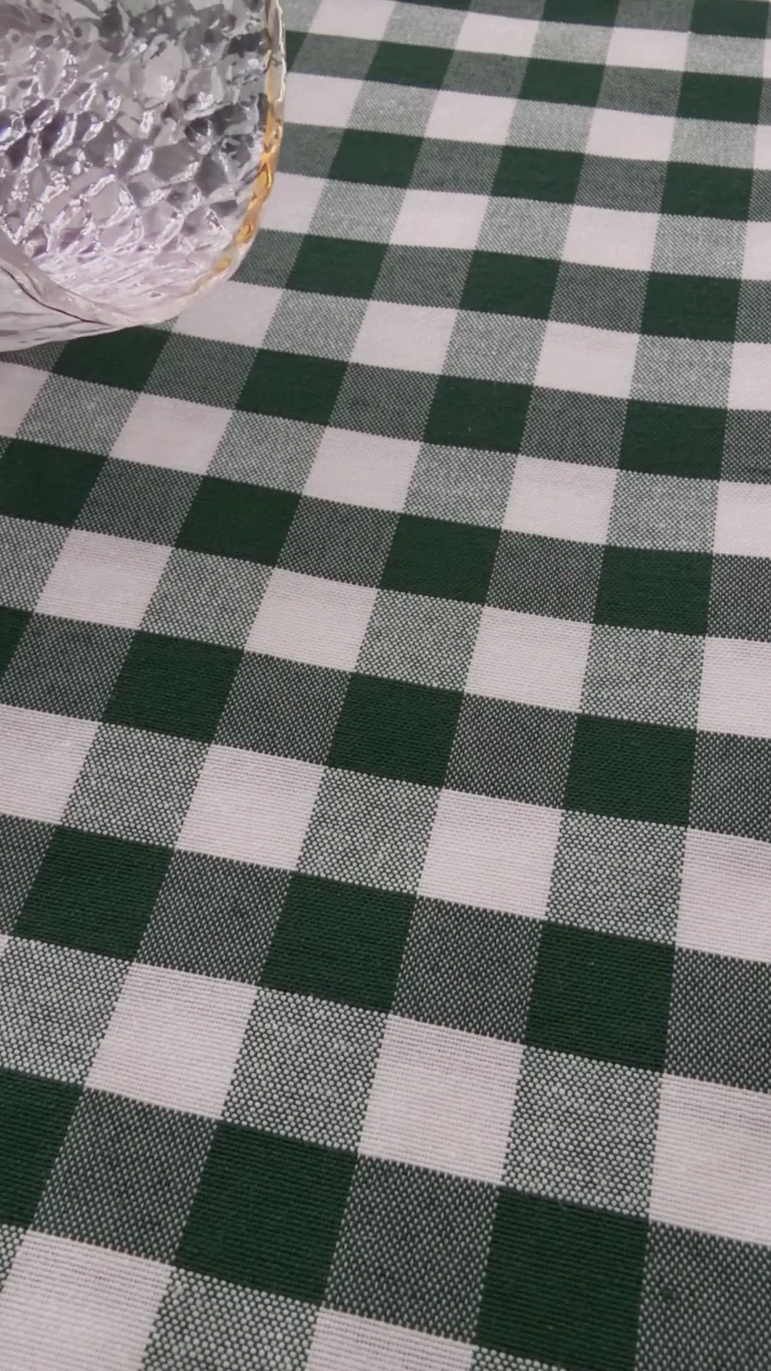 Green gingham water repellent tablecloth demonstration showing water beading on the fabric and being wiped away.